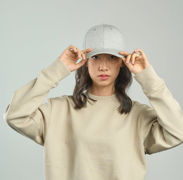 Woman wearing a light grey cap and beige sweatshirt, adjusting the brim – ideal for custom branded caps, streetwear promotions, and casual club uniforms with no minimum order in Australia.