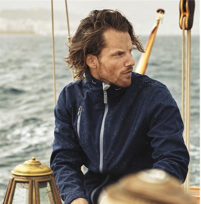 **Alt Text:** Man wearing navy custom sports jacket on a boat in wet weather – water-resistant teamwear with free logo included, ideal for clubs, events, and outdoor activities.