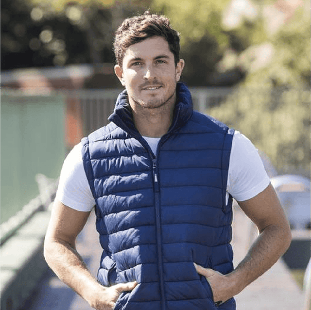 **Alt Text:** Man wearing royal blue custom puffer vest outdoors – personalised corporate vest with free logo included, ideal for staff uniforms and business branding.