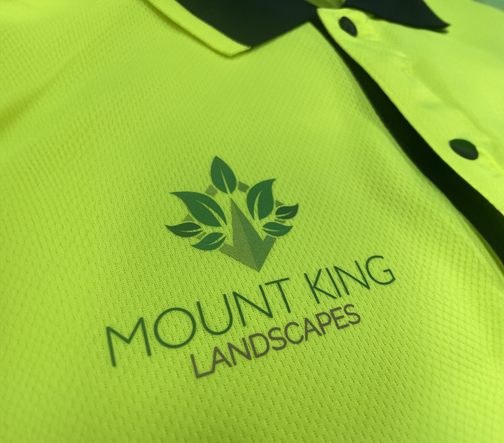 Close-up of a high-visibility yellow work shirt with the Mount King Landscapes logo printed on the chest, featuring a leaf and mountain design.