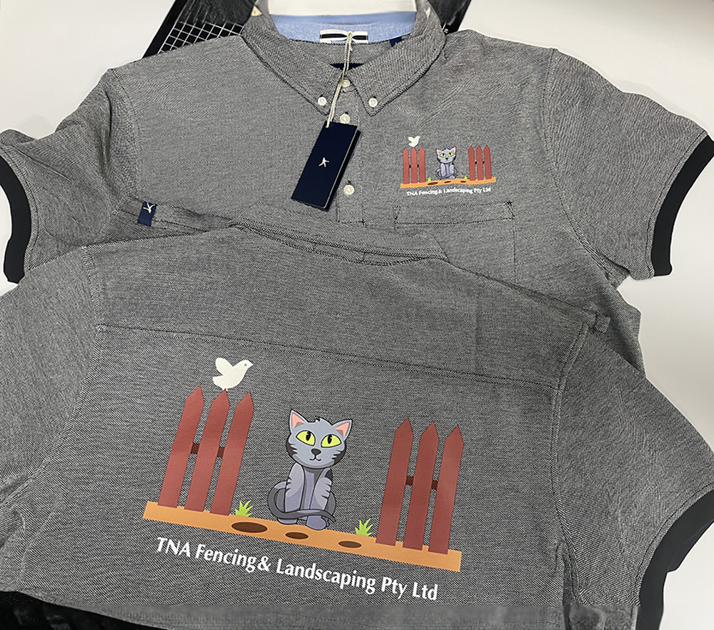 Custom grey polo shirts featuring the TNA Fencing & Landscaping Pty Ltd logo with a cartoon cat, picket fence, and white bird, printed on the chest and back.