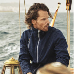 **Alt Text:** Man wearing navy custom sports jacket on a boat in wet weather – water-resistant teamwear with free logo included, ideal for clubs, events, and outdoor activities.