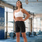 **Alt Text:** Woman standing confidently in gym wearing black activewear shorts – custom sports shorts with free logo included, ideal for fitness teams and events.