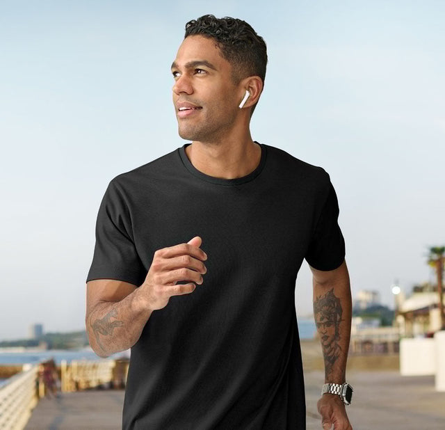 **Alt Text:** Man running along the beach wearing black custom T-shirt – personalised activewear with free logo included, perfect for events, teams, and casual uniforms.