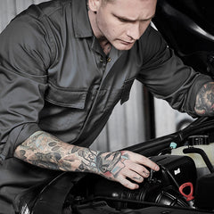 Mechanic in grey protective overalls inspecting a car engine in a workshop – ideal for custom branded overalls for automotive, maintenance, and industrial teams.