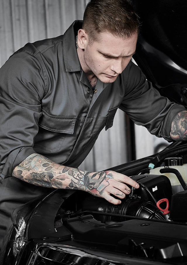 Mechanic in grey protective overalls inspecting a car engine in a workshop – ideal for custom branded overalls for automotive, maintenance, and industrial teams.