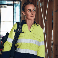 **Alt Text:** Female tradie wearing hi-vis yellow and navy work shirt with reflective tape – custom printed safety shirt with free logo included, compliant with AS/NZS standards.