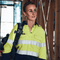**Alt Text:** Female tradie wearing hi-vis yellow and navy work shirt with reflective tape – custom printed safety shirt with free logo included, compliant with AS/NZS standards.