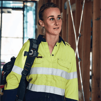 **Alt Text:** Female tradie wearing hi-vis yellow and navy work shirt with reflective tape – custom printed safety shirt with free logo included, compliant with AS/NZS standards.