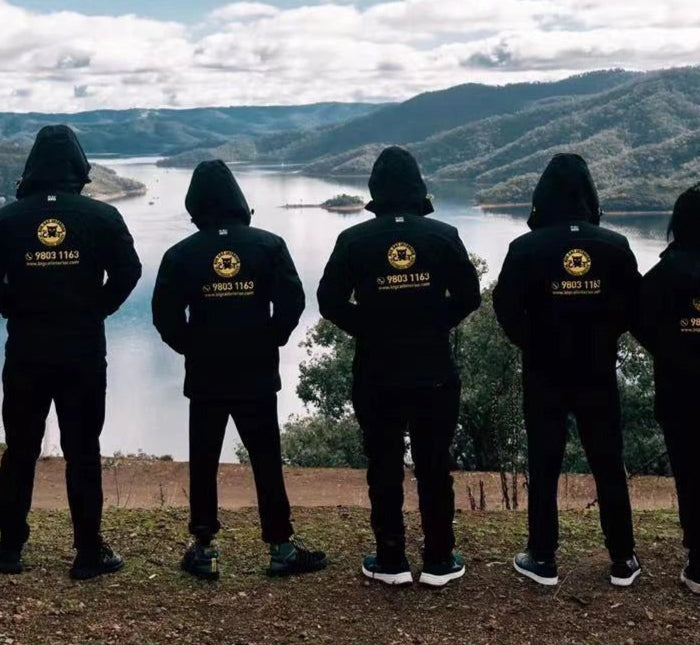 **Alt text:**  
A team wearing matching custom black hoodies with gold logos stands side by side, overlooking a scenic mountain and lake view. The branded hoodies were created by My Uniform Shop, showcasing our high-quality personalised apparel for clubs, teams, and group events across Australia. Perfect for building unity, visibility, and team spirit.