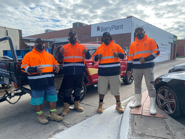 A construction crew proudly wearing custom branded hi-vis hoodies in orange and navy, standing in front of work vehicles. Designed and supplied by My Uniform Shop, showcasing high-quality, personalised workwear for Australian tradies and teams. Ideal for visibility, comfort, and team branding on the job site.
